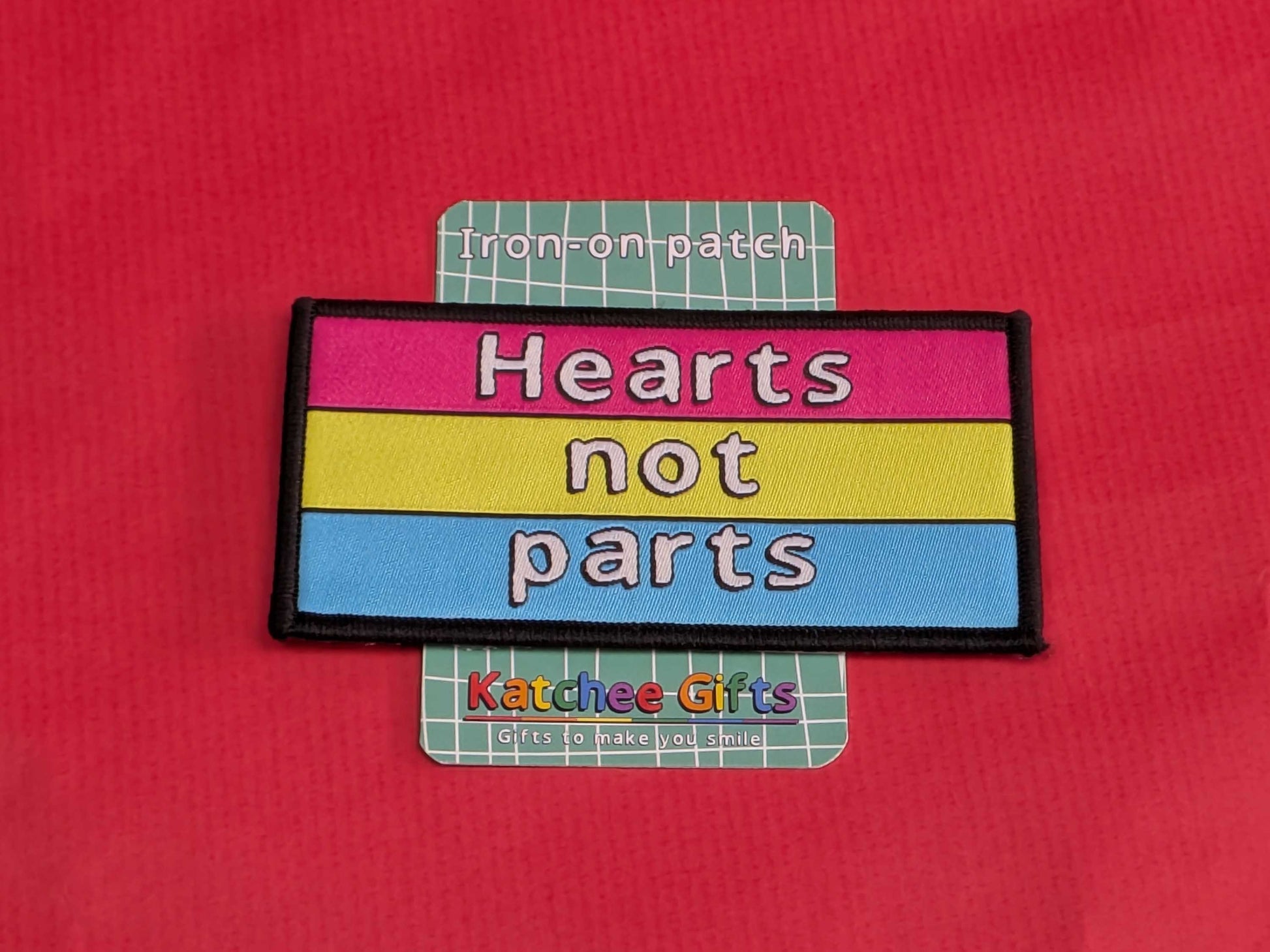 Iron-on patch with 'Hearts not parts' text on a red background, branded as Katchee Gifts.