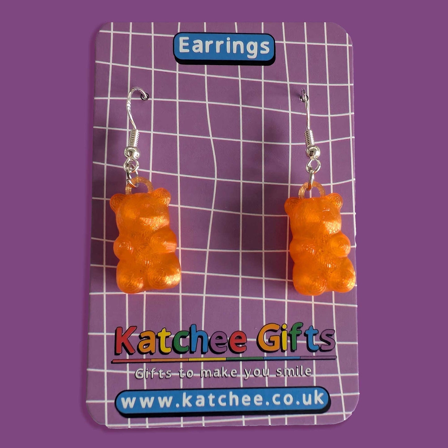 Orange gummy bear-shaped earrings on a Katchee Gifts branded card with a purple background.