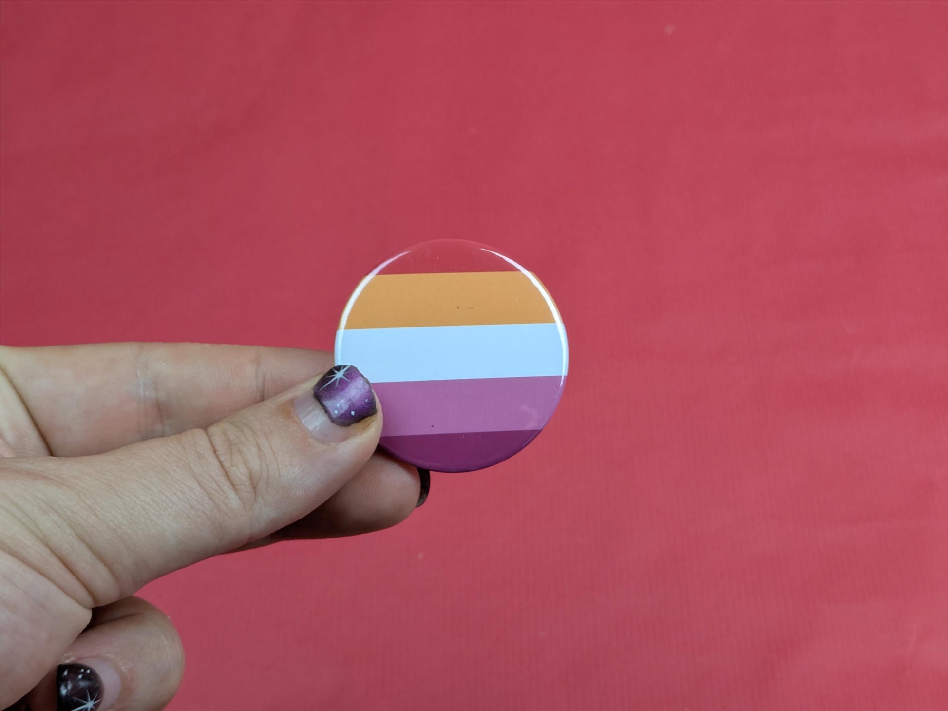 Hand holding a circular badge with the lesbian flag against a red background