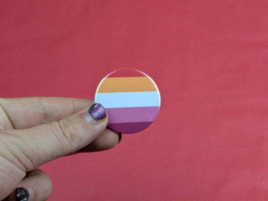 Hand holding a circular badge with the lesbian flag against a red background
