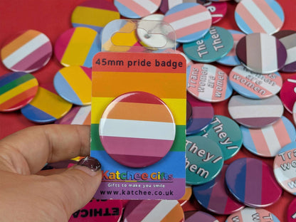 Packaged lesbian pride badge with a hand holding it against a background of various buttons.