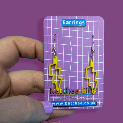 Yellow lightning bolt earrings on a purple card held by a hand against a purple background