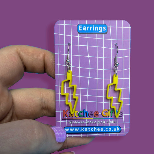Yellow lightning bolt earrings on a purple card held by a hand against a purple background