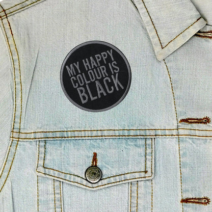 A circular black patch with the text 'MY HAPPY COLOUR IS BLACK' in gray lettering, shown on the chest of a light blue denim jacket.