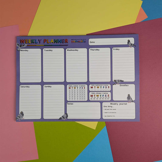 A weekly planner pad with a purple border and white writing sections, photographed flat on a colorful geometric paper background.