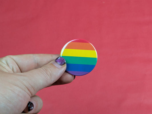 Hand holding a rainbow striped button badge against a red background