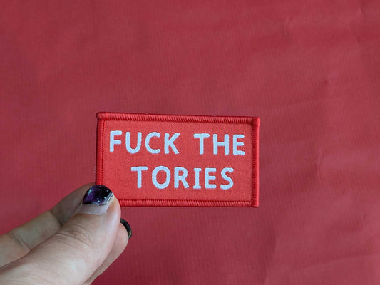 Red patch with white text 'FUCK THE TORIES' held against a red background