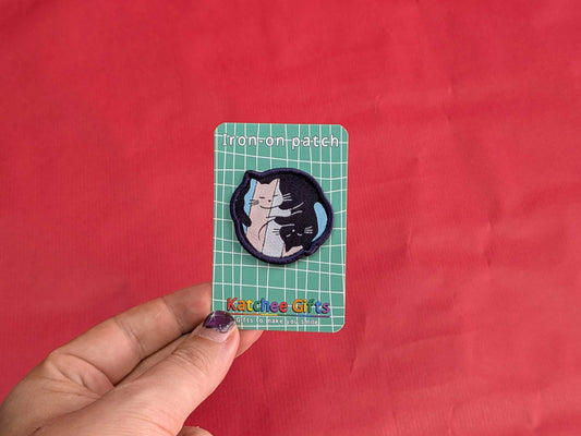 Cat-themed patch on a green grid card held against a red background