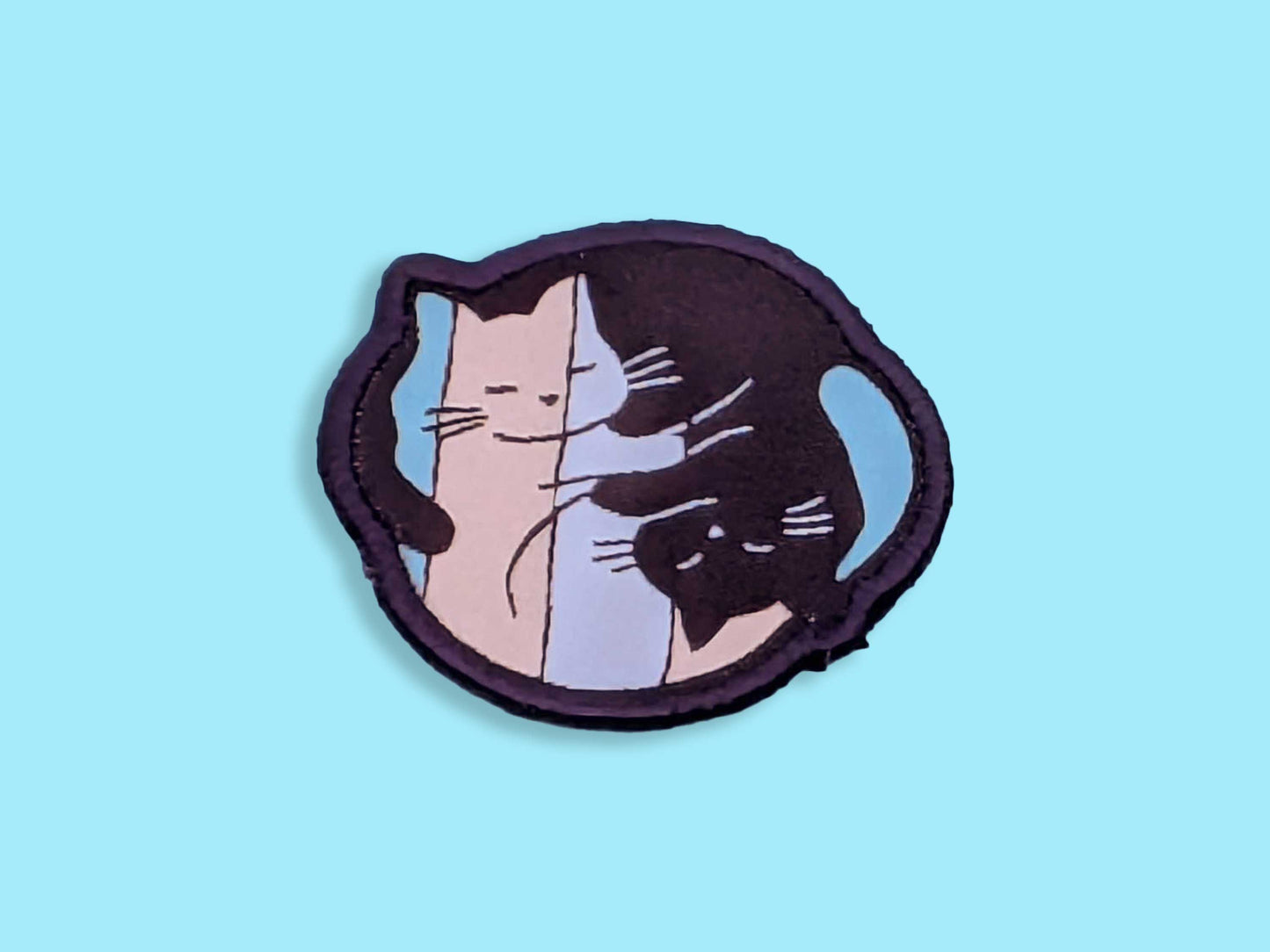 Patch with a ying yang style cat design in the trans flag colours