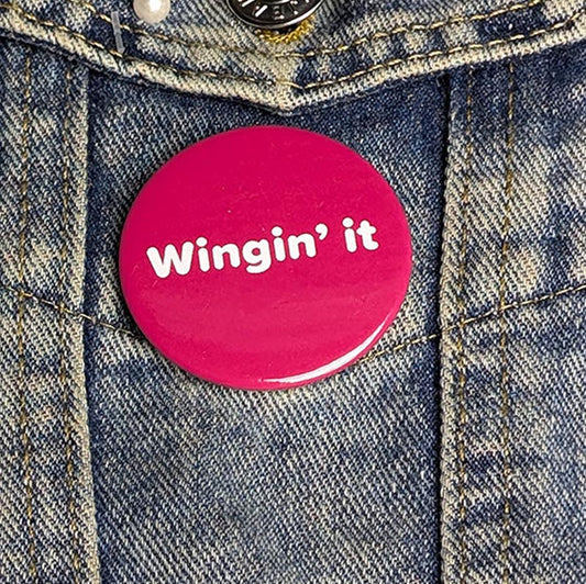 Pink button with 'Wingin' it' text on a denim jacket